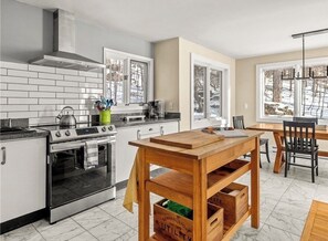 A kitchen with a stove, oven, and wooden table with storage drawers. - The Pond House: Cozy Home with a View, Swimming Pond, and Hot Tub, Pet-Friendly! (Margaretville)