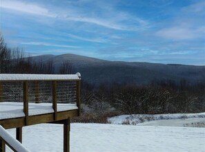 A wooden deck with snow on the railings, overlooking a snowy landscape with distant hills. - The Pond House: Cozy Home with a View, Swimming Pond, and Hot Tub, Pet-Friendly! (Margaretville)
