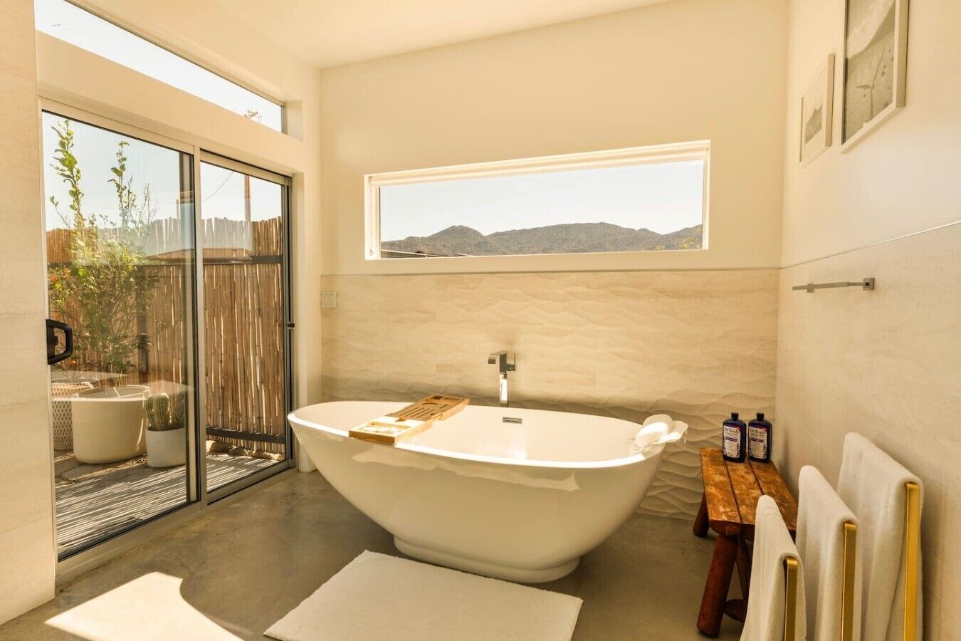 A modern bathroom with a freestanding bathtub, a window with a mountain view, and a wooden bench.