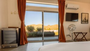 Een slaapkamer met een groot bed, een televisie, een airconditioner en uitzicht op een woestijnlandschap.