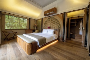 Un dormitorio con una cama grande, suelo de madera, un armario y una ventana con vistas a árboles.