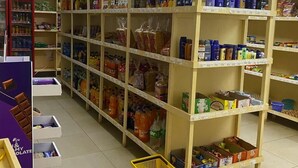 A grocery store with shelves stocked with various products, a yellow basket on the floor, and a purple display counter.