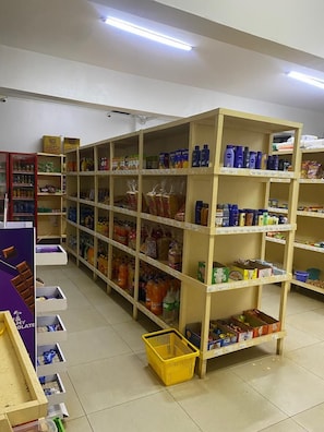 A grocery store with shelves stocked with various products, a yellow basket on the floor, and a purple display counter. - Awesome studio with fitness place,parking and good security. (Nairobi)
