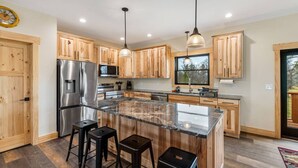 Une cuisine moderne avec des meubles en bois, des appareils électroménagers en acier inoxydable, un îlot en granit et des tabourets de bar.
