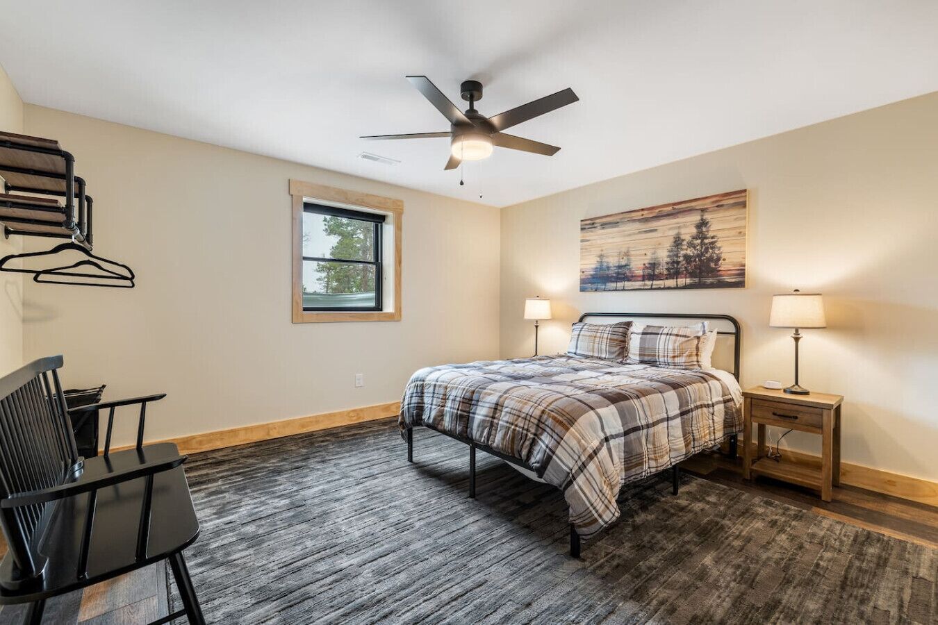 A bedroom with a bed, a desk, a chair, a ceiling fan, a window, and a painting on the wall.