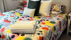 Een bed met een kleurrijke bloemenbedekking, een geborduurd kussen en een opgevouwen plaid.