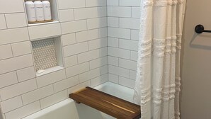 Een moderne badkamer met een witte badkuip, een houten plank met toiletartikelen en een douchegordijn.