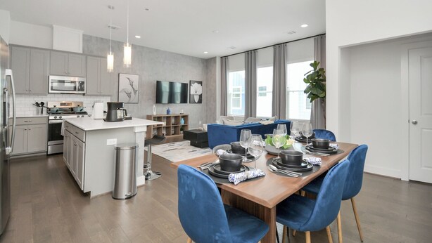 Une cuisine moderne avec des meubles gris, un îlot central et un coin repas avec des chaises bleues et une table en bois, le tout disposé pour accueillir quatre personnes.