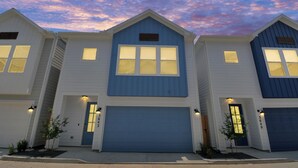 Une rangée de maisons de ville à trois étages, chacune dotée d’un garage, d’un porche et d’un petit arbre dans le jardin avant.