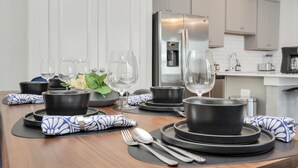 Une cuisine moderne équipée d’appareils électroménagers en acier inoxydable, avec une table à manger dressée avec de l’assiette, des bols et des couverts noirs et blancs.