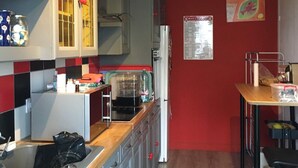 Eine kleine Küche mit roter Wand, einem weißen Kühlschrank, einem Spülbecken und einer Essecke mit Tisch und Stühlen.