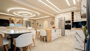 Een moderne keuken met een marmeren kookeiland, inbouwapparatuur en een eethoek met witte stoelen en een glazen tafel.