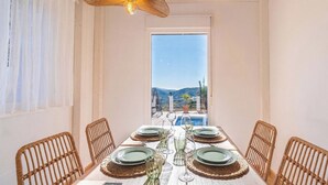 A dining table set for six with wicker chairs, a view of mountains and a pool through a large window. - Villa María Sayalonga by Ruralidays (Málaga)