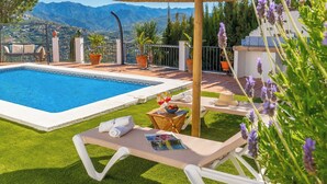 A poolside area with a clear view of mountains, a lounge chair, a table with a drink, and potted plants. - Villa María Sayalonga by Ruralidays (Málaga)