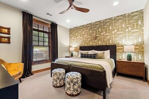 A bedroom with a bed, two ottomans, a nightstand, a lamp, a ceiling fan, and a window with blinds. - Newly Renovated! Walk-In Condo on Lake Taneycomo! (Branson)
