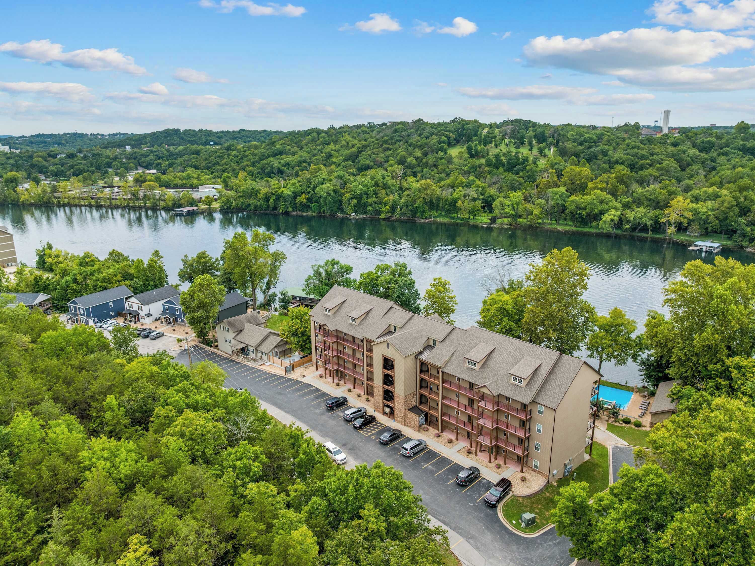 A multi-story hotel with a parking lot and a view of a lake.