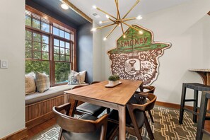A dining area with a wooden table, chairs, and a bench with cushions. A decorative wall piece with the word 'SMOKEY' is visible. - Newly Renovated! Walk-In Condo on Lake Taneycomo! (Branson)