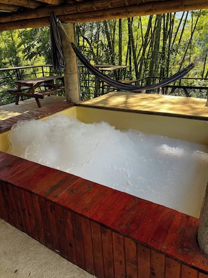 Ein Whirlpool mit Holzrand, eine Hängematte und ein Picknicktisch inmitten eines Bambuswaldes.