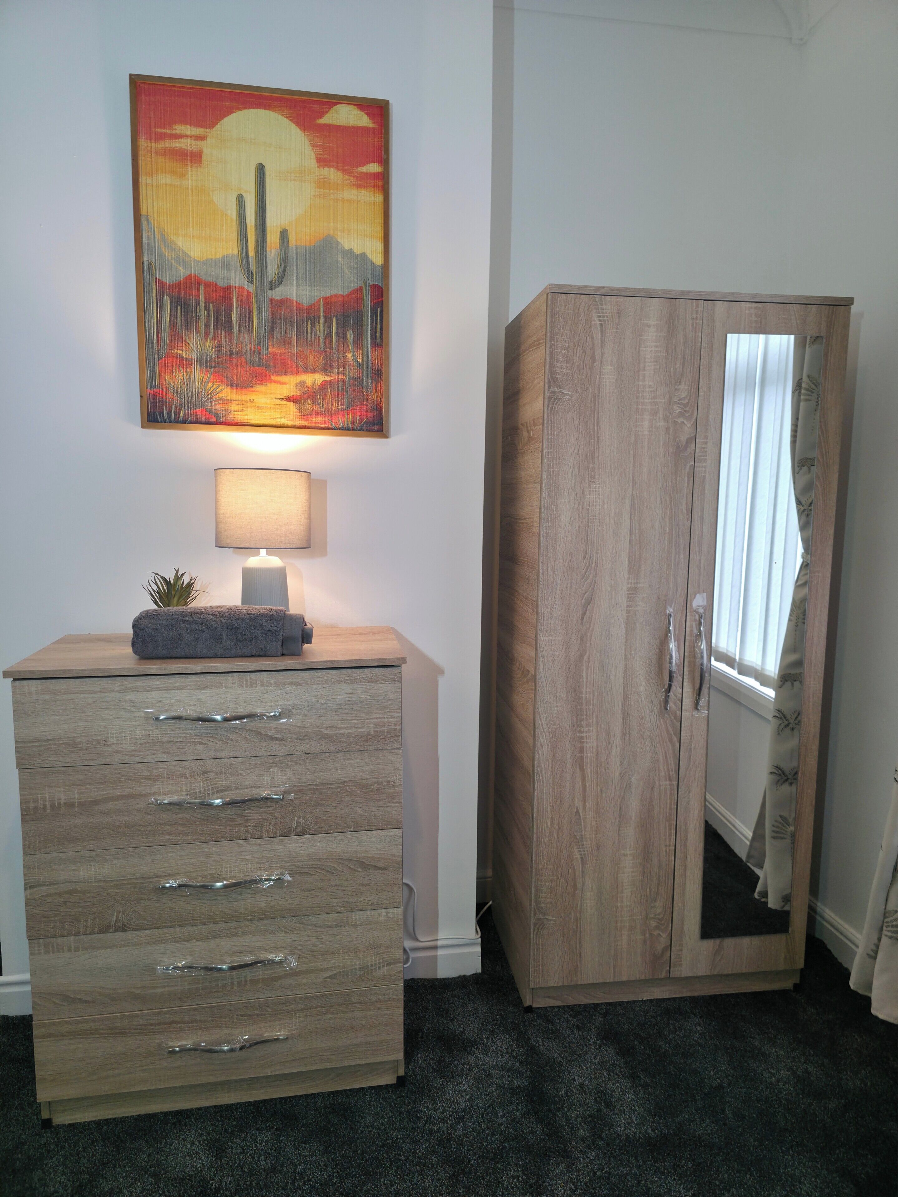 Une pièce comprenant une commode en bois, une lampe et un tableau représentant un paysage désertique.