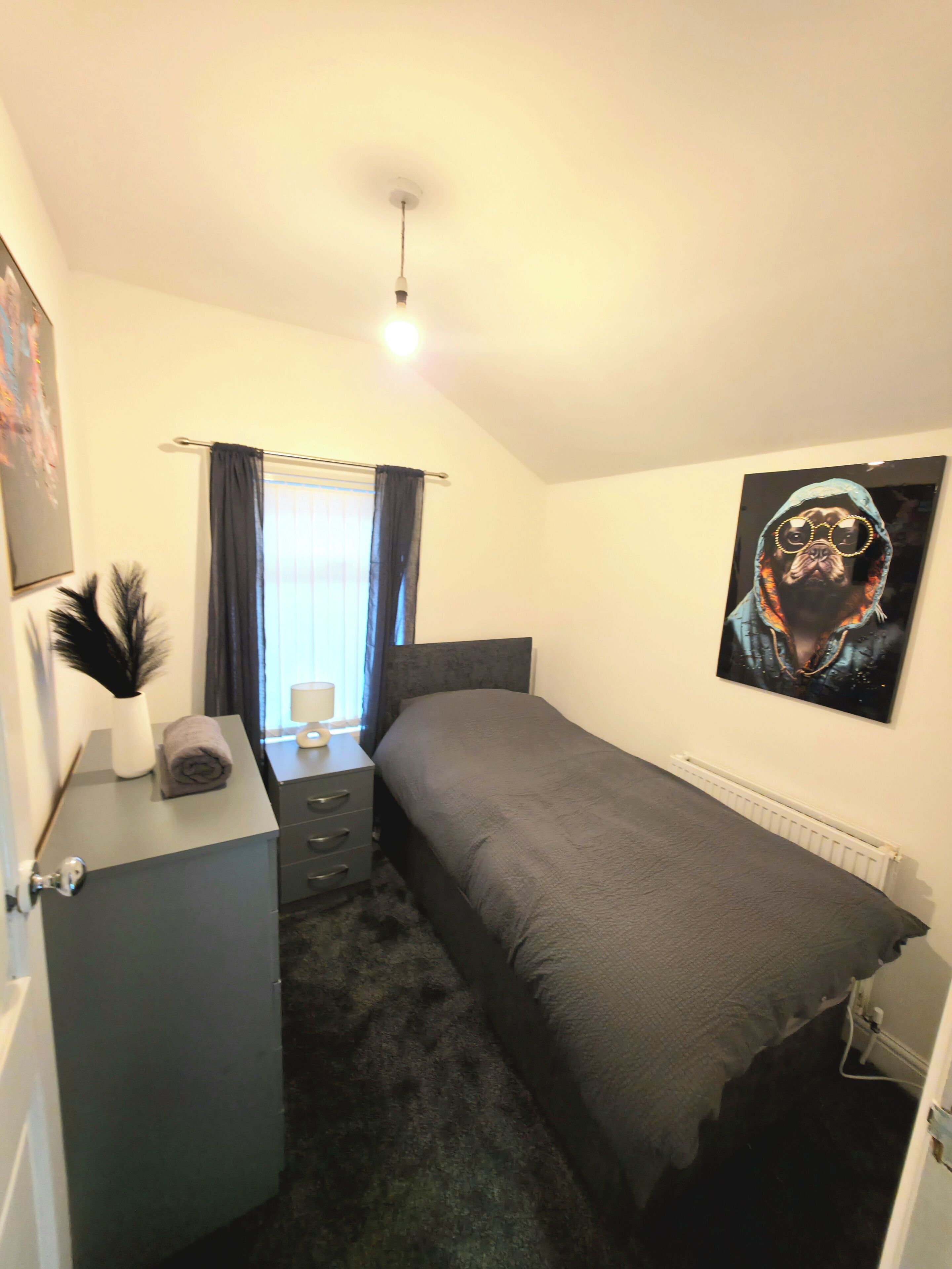 A bedroom with a bed, a desk, a radiator, and a poster on the wall.