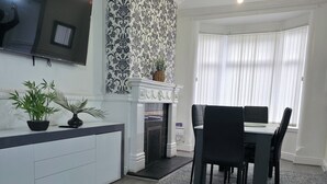 A modern living room with a fireplace, dining area, and a flat-screen TV mounted on the wall. - Costa Home Middlesbrough (Middlesbrough)