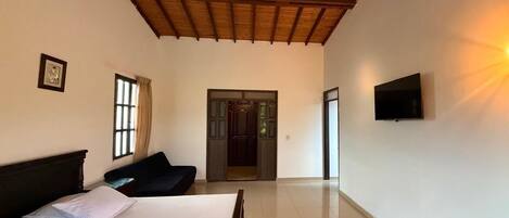 A bedroom with a bed, a TV, a door, and a window.