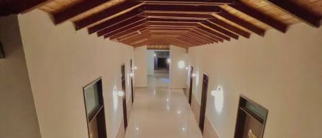 A hallway with a wooden ceiling, a polished floor, and wall-mounted light fixtures.