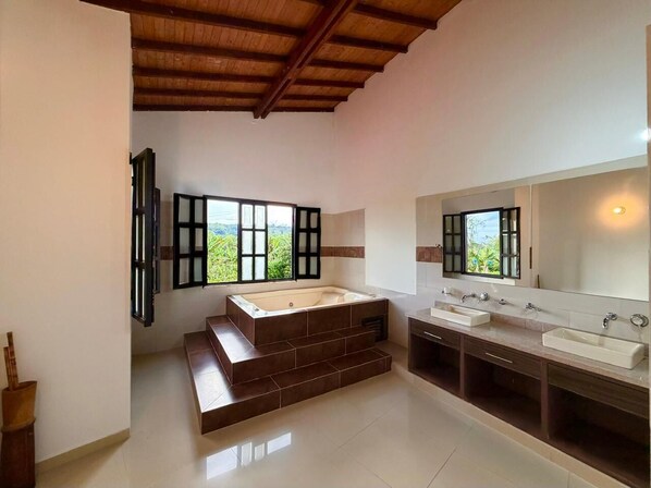 A modern bathroom with a large bathtub, two sinks, and a window with a view.