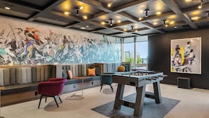 Un espacio interior moderno con mesa de fútbol de mesa, zona de estar con bancos acolchados y un gran mural abstracto en la pared.
