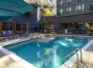 Ein Swimmingpool mit Liegestühlen und Sonnenschirmen, umgeben von einem modernen Gebäude mit Balkonen.