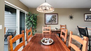 A dining room with a wooden table, six chairs, a hanging light fixture, a potted plant, and two framed pictures on the wall. - Marina Cay Condo Retreat (Bigfork)