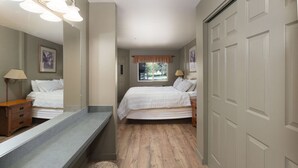 A bedroom with a bed, a dresser, a vanity with a mirror, a window with curtains, and a door. - Marina Cay Condo Retreat (Bigfork)