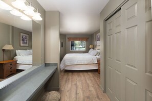 A bedroom with a bed, a dresser, a vanity with a mirror, a window with curtains, and a door. - Marina Cay Condo Retreat (Bigfork)
