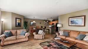 A living room with two sofas, a coffee table, and a dining area with chairs and a table. - Marina Cay Condo Retreat (Bigfork)