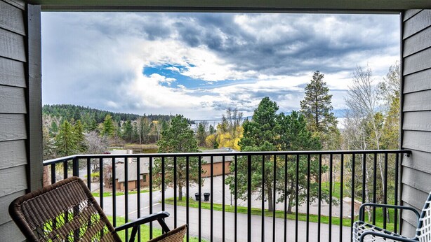 A balcony with a view of a parking lot, trees, and a cloudy sky. - Marina Cay Condo Retreat (Bigfork)