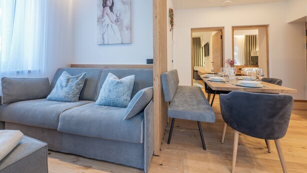 A modern living room with a grey sofa, a dining table set for four, and a large mirror.