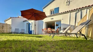 Una casa con patio, mobiliario exterior y un gran paraguas.