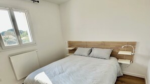 Un dormitorio con cabecera de madera, cama con ropa de cama blanca, ventana con vista y un radiador.