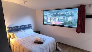 Une chambre à coucher avec un lit, une fenêtre donnant sur la ville, une table de chevet et un climatiseur fixé au mur.