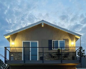 Een huis met twee verdiepingen, een balkon, een gevel van natuursteen en een plat dak.