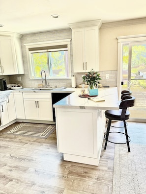 Een moderne keuken met witte kasten, een groot eiland en uitzicht op de omgeving.