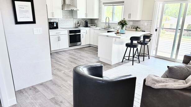 A modern kitchen with white cabinetry, a central island, and a dining area with black bar stools. - FIFA Fans! Brand-NEW 1 Bedroom, 1 Bath Apartment  (San Jose)