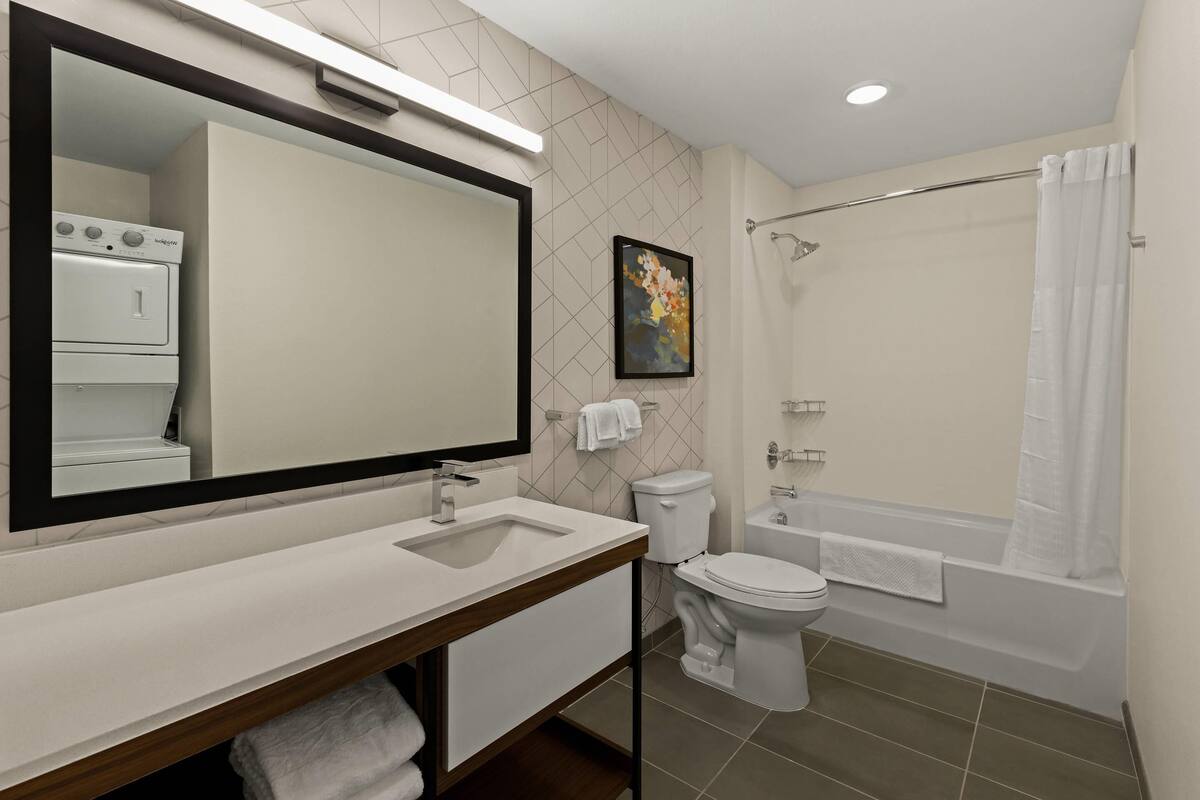 Une salle de bain moderne avec un grand miroir, un lavabo, des toilettes et une baignoire.
