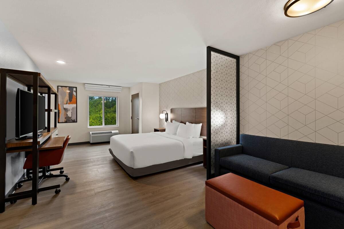 Une chambre d’hôtel comprenant un lit, un bureau avec un ordinateur, un canapé et un banc.