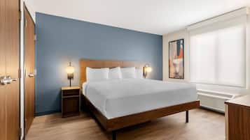 Habitación de hotel con cama de madera, dos lámparas de noche, una mesita de noche, ventana con persianas y aire acondicionado instalado en la pared.