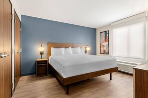 Ein Hotelzimmer mit einem Holzbett, zwei Nachttischlampen, einem Nachttisch, einem Fenster mit Jalousien und einer Wand-Klimaanlage.