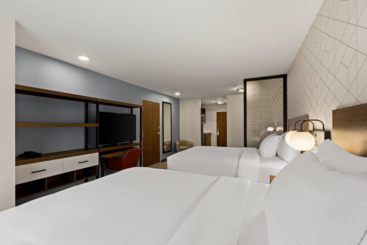Une chambre d’hôtel avec deux lits, un bureau avec une télévision et une armoire.