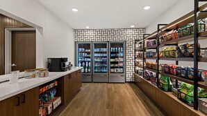 Una cocina moderna y limpia con armarios de madera, encimera blanca y una cafetera. Hay tres refrigeradores llenos de bebidas y aperitivos.