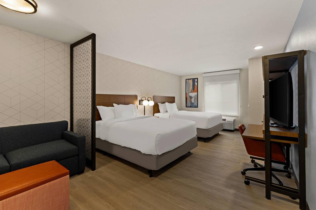 Une chambre d’hôtel avec deux lits, un canapé, un bureau et une télévision.