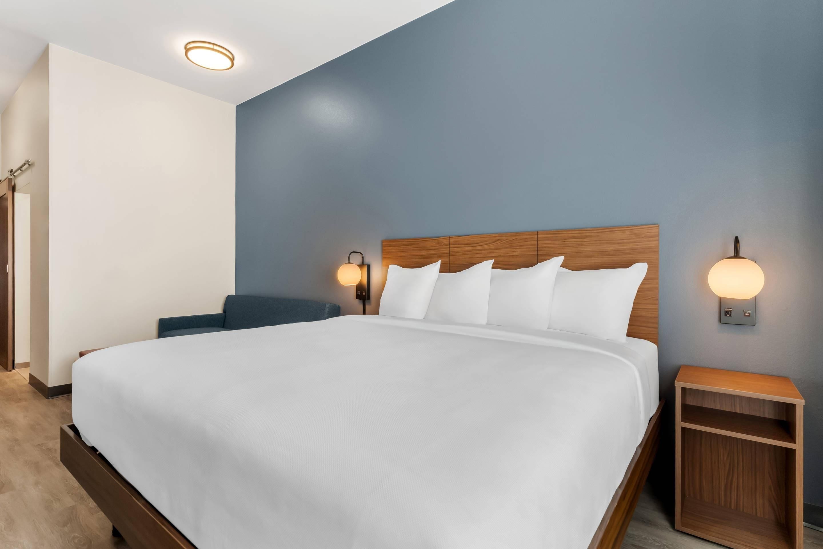 A modern hotel room with a large bed, two bedside tables, and a wooden headboard.